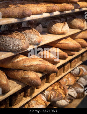 Du pain frais sur des étagères de boulangerie. La diversité du pain dans une lumière vive. Pains avec une croûte dorée sur des étagères en bois. Pains assortiment. Banque D'Images