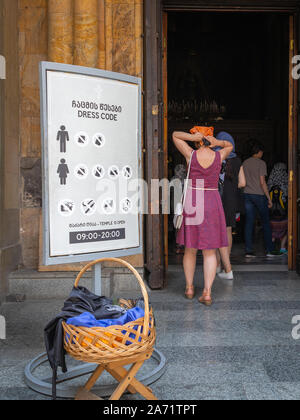 Tbilissi, Géorgie - 21 juillet 2019 : qui entre dans la Cathédrale Sioni après avoir lu et suivi le code vestimentaire règlement comme indiqué sur l'affichage Banque D'Images