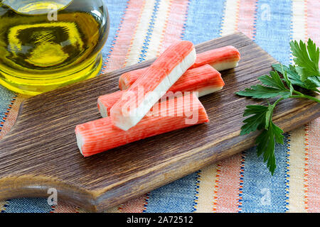 Les bâtonnets de crabe surimi et le persil sur une planche à découper brun près de pot avec de l'huile d'olive. Les fruits de mer et d'ingrédients pour les salades. Une saine alimentation et faire cuire à la maison. Banque D'Images