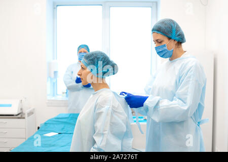 Une infirmière robes une chirurgien dans un costume stérile avant la chirurgie. Banque D'Images