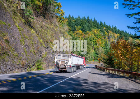 Rouge industriels les gros camion camion semi remorque semi vrac long avec avec trois axes fonctionnant en descente sur la sinueuse route d'automne avec rock mountain vues Banque D'Images