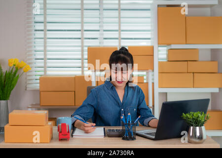 Charmante belle asiatique propriétaire adolescent femme d'affaires travailler à la maison pour faire des achats en ligne, l'écriture l'ordre sur son portable à l'ordinateur portable avec office rad Banque D'Images