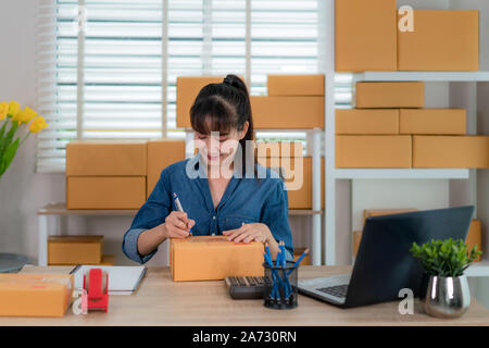 Charmante belle asiatique propriétaire adolescent femme d'affaires travailler à la maison pour faire des achats en ligne, l'écriture adresse en boîte aux lettres avec un ordinateur portable avec l'équipement de bureau, Banque D'Images