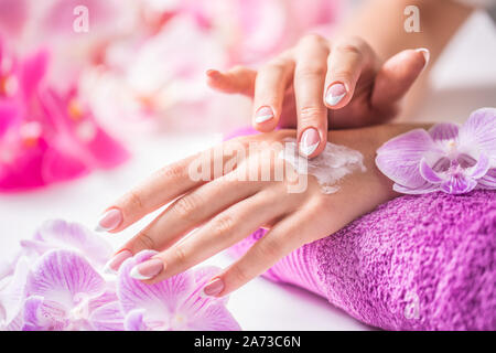 Belles femmes l'application de crème grasse. Orchidée pourpre serviette et décoration. Concept Santé - Ongles soins de la peau bien-être et spa Banque D'Images