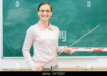 Friendly teacher standing in front of blackboard en classe Banque D'Images