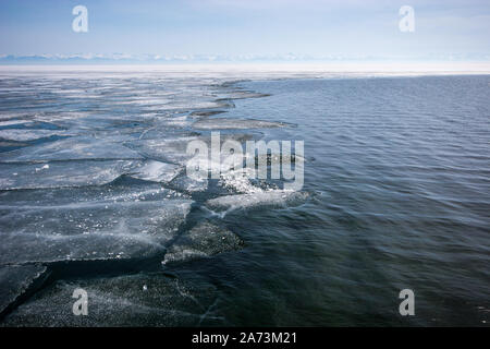 Lac Baikal en hiver avec de l'eau libre et le bord de la glace brisée. Une chaîne de montagnes à l'horizon. Banque D'Images