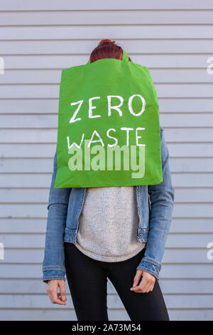 Une jeune fille se tient avec un sac eco textiles suspendus avec l'inscription zéro déchets sur sa tête qui lui couvre le visage. Fille dans une veste en jean avec ses mains d Banque D'Images