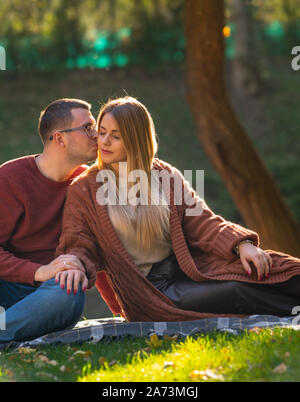 Belle jeune femme d'être embrassé par son petit ami sur une soirée romantique dans un parc comme ils vous détendre sur un tapis sur l'herbe Banque D'Images