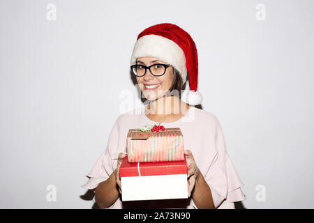 Portrait of young woman in Santa hat holding Christmas presents and smiling at camera contre le fond blanc Banque D'Images