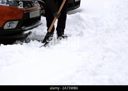 Le brossage et l'homme de pelleter la neige voiture orange en hiver après des chutes de neige. Pelle à main. Problèmes d'hiver des automobilistes. Banque D'Images