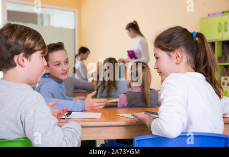 Les élèves heureux assis bavardant à l'arrière des bureaux, à l'enseignement à l'école élémentaire Banque D'Images