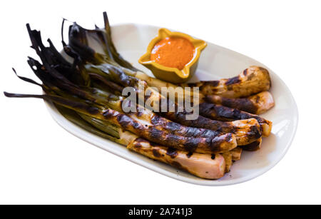 Oignons rôtis Calcots servi sur assiette avec la sauce Romesco - hiver catalan traditionnel plat. Plus isolé sur fond blanc Banque D'Images