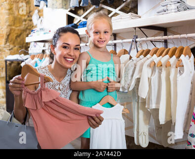 Cheerful femelle avec petite fille choisir robe rose en boutique vêtements pour enfants Banque D'Images