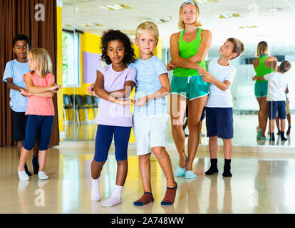 Groupe d'enfants joyeux heureux vigoureux mouvements dans la pratique de classe de danse jive avec entraîneur féminin Banque D'Images