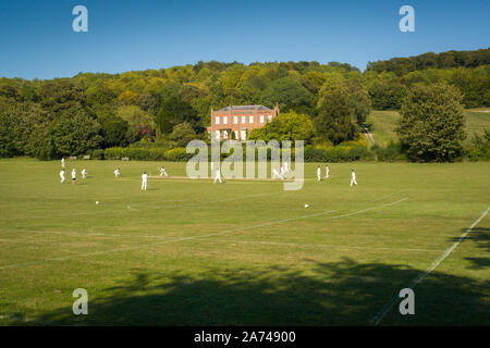 Un match de cricket de village à Hambleden, Buckinghamshire avec la maison Kenricks classée Grade II derrière, construite en 1725 Banque D'Images