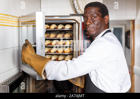 Portrait of African American Baker le contrôle de processus de cuisson du pain dans un four professionnel à bakery Banque D'Images