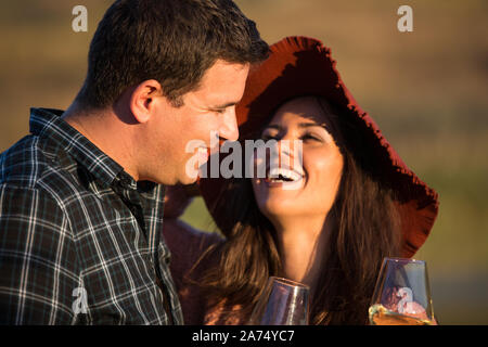 Portrait de couple avec un grand sourire au coucher du soleil avec le lac derrière eux au milieu d'un vignoble. Banque D'Images