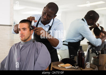 Jeune homme obtenir même avec electric clipper par des professionnels de coiffure africaine à salon Banque D'Images