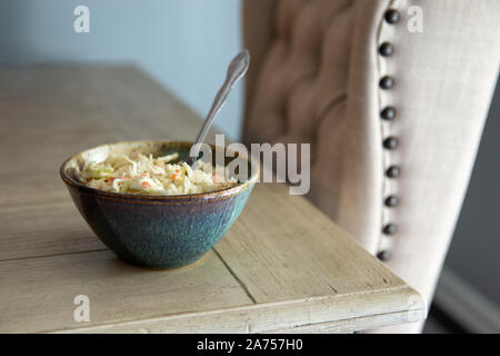 Vue latérale de la poterie bol rempli avec de la salade de chou sur une table en bois blanc et d'un fauteuil rembourré. Banque D'Images