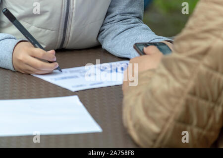 L'enfant dessine avec un stylo-feutre sur une feuille de papier posé sur la table. Au contraire, un adulte est titulaire d'un smartphone. Vue de face. Banque D'Images