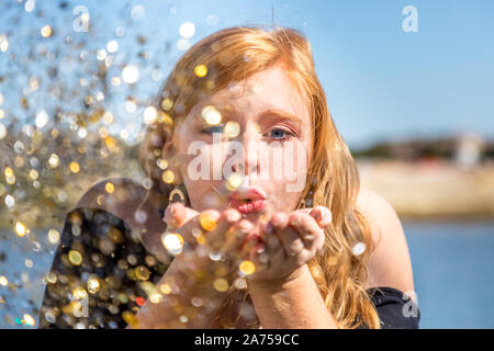 Close up portrait of attractive young woman blowing paillettes. Modèle des femmes de race blanche aux cheveux rouges s'amuser en plein air Banque D'Images