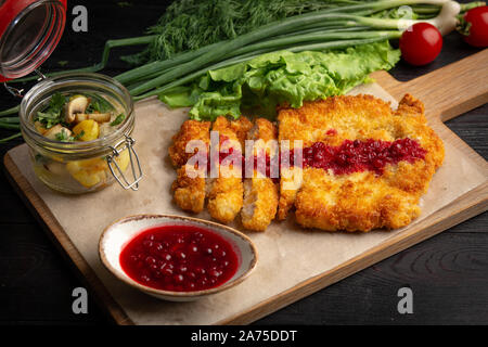 Escalope de poulet sur une planche avec des fines herbes et sauce aux airelles dans une tasse, servi avec pommes de terre sautées aux champignons Banque D'Images
