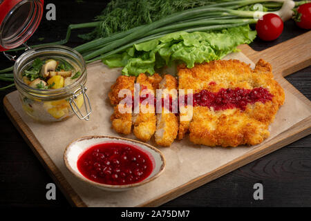 Escalope de poulet sur une planche avec des fines herbes et sauce aux airelles dans une tasse, servi avec pommes de terre sautées aux champignons Banque D'Images