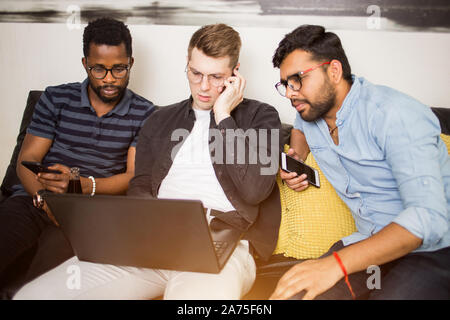 Les jeunes entrepreneurs à la recherche d'idées pour les entreprises, à l'aide d'ordinateur portable et les smartphones, appelant à des clients potentiels ou partenaires. Amis multi ethnic sitti Banque D'Images