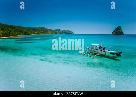 El Nido island hopping voyage. Bateau amarré dans le calme de l'océan bleu turquoise lagon peu profond avec des ailerons de requins de l'île rocheuse forme en arrière-plan Banque D'Images