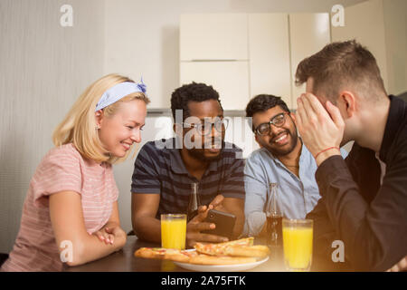 Beautiful happy young caucasian woman à table avec ses amis, riant looking at smartphone. L'essai de nouveaux étudiants ethniques multiples gadg Banque D'Images