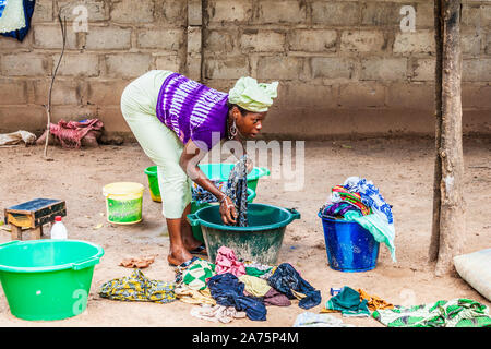 Une jeune femme gambienne vêtements lavage des mains dans la cour d'un village composé en Sénégambie. Banque D'Images