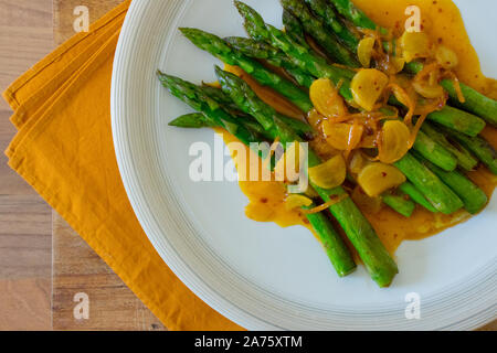 La photographie culinaire d'asperges sautées vert sur une plaque blanche avec orange et sauce à l'ail. Banque D'Images