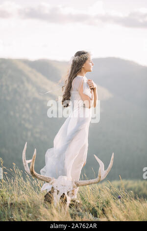 Belle femme de sveltes figure dans une longue robe de tulle, profil sinueux, voile, nature, montagne, forêt, le chevreuil crâne avec cornes près du pied, brid Banque D'Images