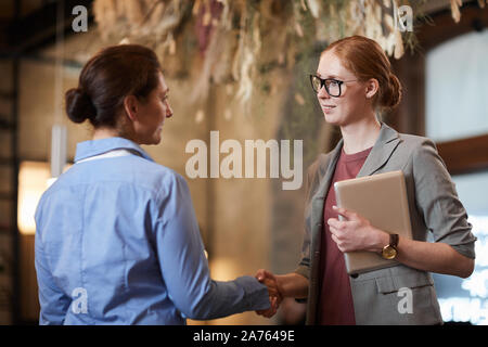 Two businesswomen shaking hands et permanent de l'autre message d'avant la réunion Banque D'Images