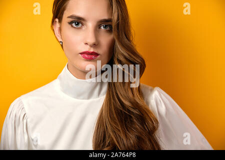 Fermer portrait d'une belle jeune fille avec boucles et le rouge à lèvres rouge dans un chemisier blanc sur fond jaune. Banque D'Images