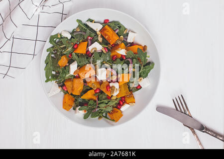 Salade de potiron de roquette, feta et graines de grenade en plaque blanche sur fond de bois blanc, vue du dessus. Banque D'Images