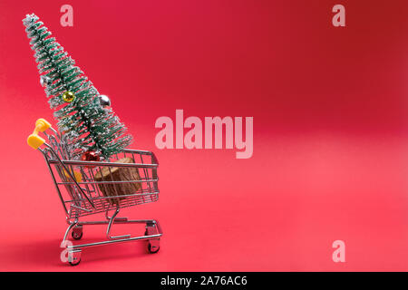 Artifitial petit arbre de Noël dans un panier sur fond rouge. Shopping, acheter des cadeaux pour les vacances d'hiver. Banque D'Images