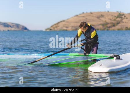 Sportsman préparer son matériel de planche à voile dans les eaux peu profondes. Banque D'Images