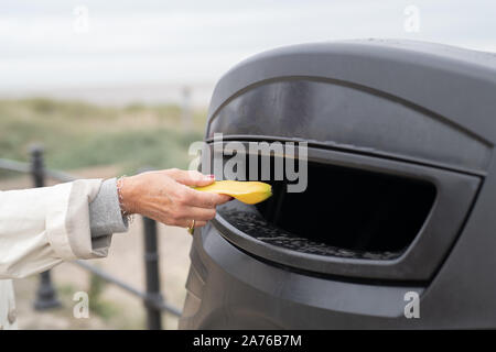 Personne qui met une peau de banane dans la poubelle publique extérieure Banque D'Images