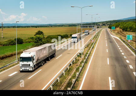 Camions Camion blanc en ligne qu'une caravane ou d'un convoi sur la route de pays sous un beau ciel Banque D'Images