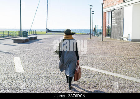 Titel Woman wearing headscarf marcher par ocean with briefcase Banque D'Images