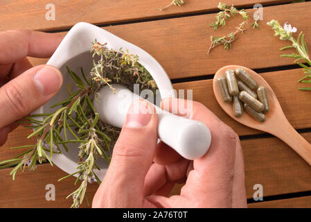 Des mains des médecines naturelles dans un mortier en céramique blanche avec cuillère en bois avec des capsules et des plantes. La médecine naturelle Alternative concept. À Banque D'Images