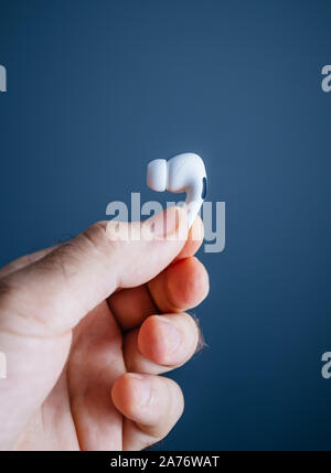 Paris, France - Oct 30, 2019 : Man hand holding dernières nouveaux ordinateurs Apple AirPods Pro casque avec suppression du bruit active pour un son enveloppant - fond gris isolé - vue latérale Banque D'Images