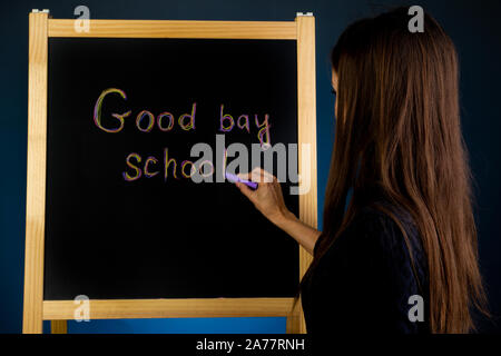 Femme écrit sur le tableau noir à la craie l'inscription de l'école Au revoir Banque D'Images