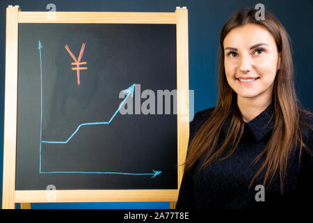 La courbe de l'yen japonais est dessiné sur un tableau noir, avec une femme debout à proximité. Le marché financier change Banque D'Images