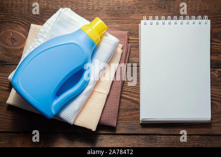 L'offre de lavage, adoucisseur, détergent, linges à vaisselle et le bloc-notes page blanche sur table en bois. Conseils à la personne des maquettes. Banque D'Images