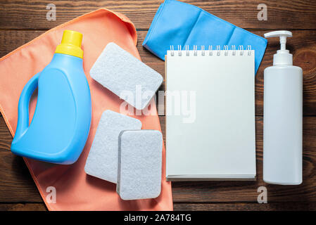 L'offre de lavage, adoucisseur, détergent, linges à vaisselle et le bloc-notes page blanche sur table en bois. Conseils à la personne des maquettes. Banque D'Images