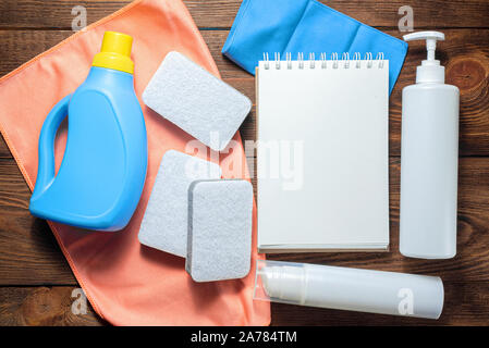 L'offre de lavage, adoucisseur, détergent, linges à vaisselle et le bloc-notes page blanche sur table en bois. Conseils à la personne des maquettes. Banque D'Images