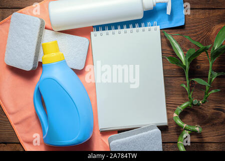 L'offre de lavage, adoucisseur, détergent, linges à vaisselle et le bloc-notes page blanche sur table en bois. Conseils à la personne des maquettes. Banque D'Images