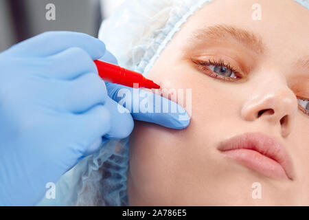 Service de cosmétologie. Jeune femme à la beauté tout en faisant mentir clinique médecin marques injectable close-up Banque D'Images